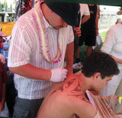 picture of Maori artist drawing an example of a tattoo on a young man's back
