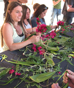 picture of ladies making lei from green leaves and bougainvillea flowers