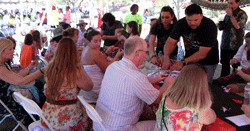 picture of lots of people under a tent learning how to string a lei